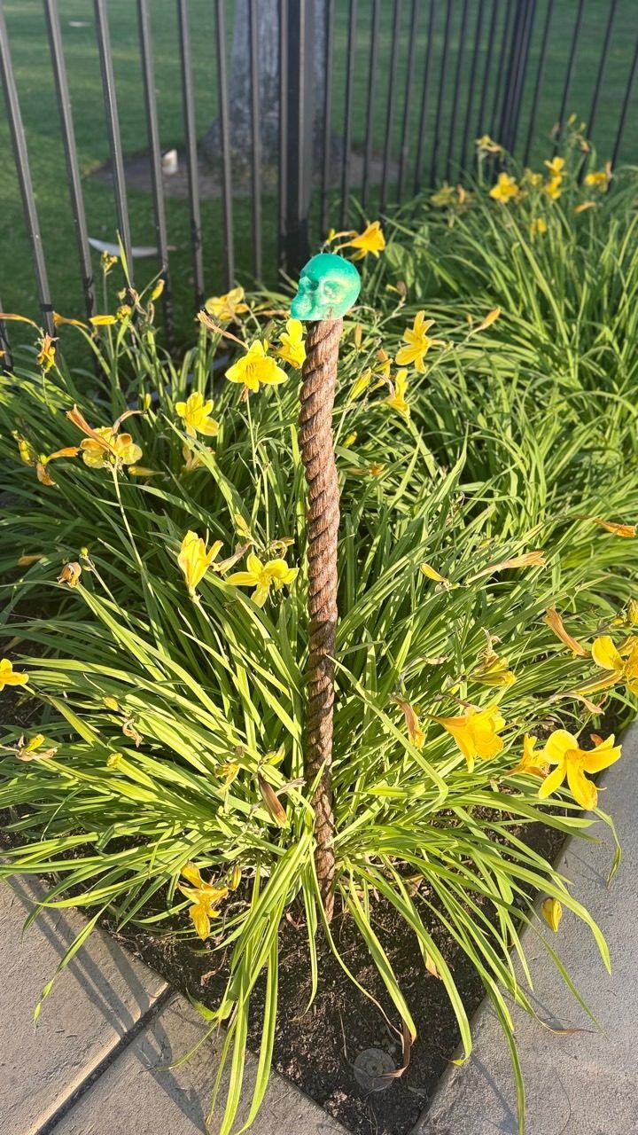 A rust-colored twisted steel walking piece topped with a small green skull among yellow flowers.
