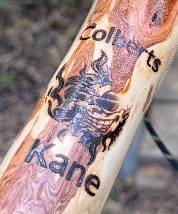 Close-up of a hand-burned name and grinning figure on a polished wood cane.