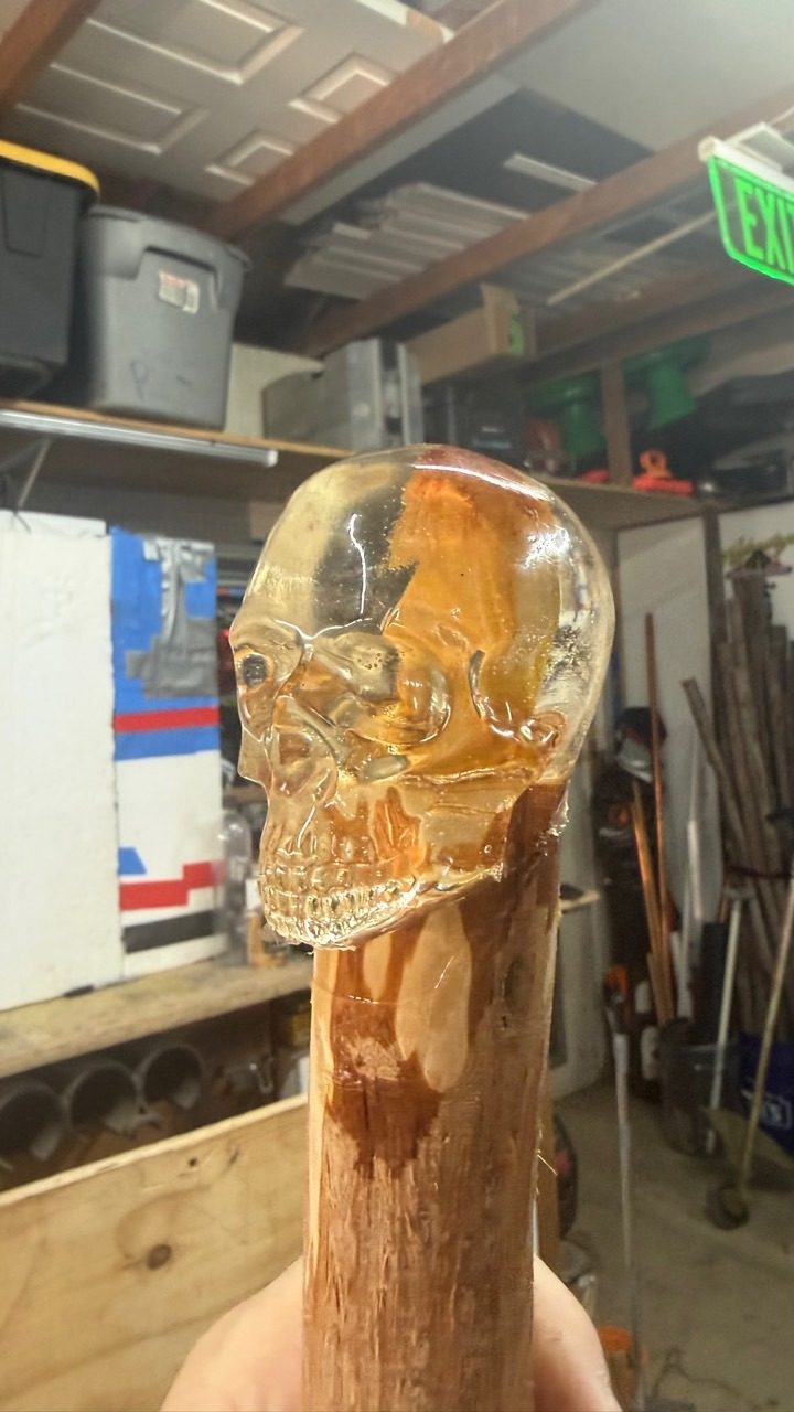 Close-up of a transparent amber resin skull fitted to a wooden walking piece inside the workshop.